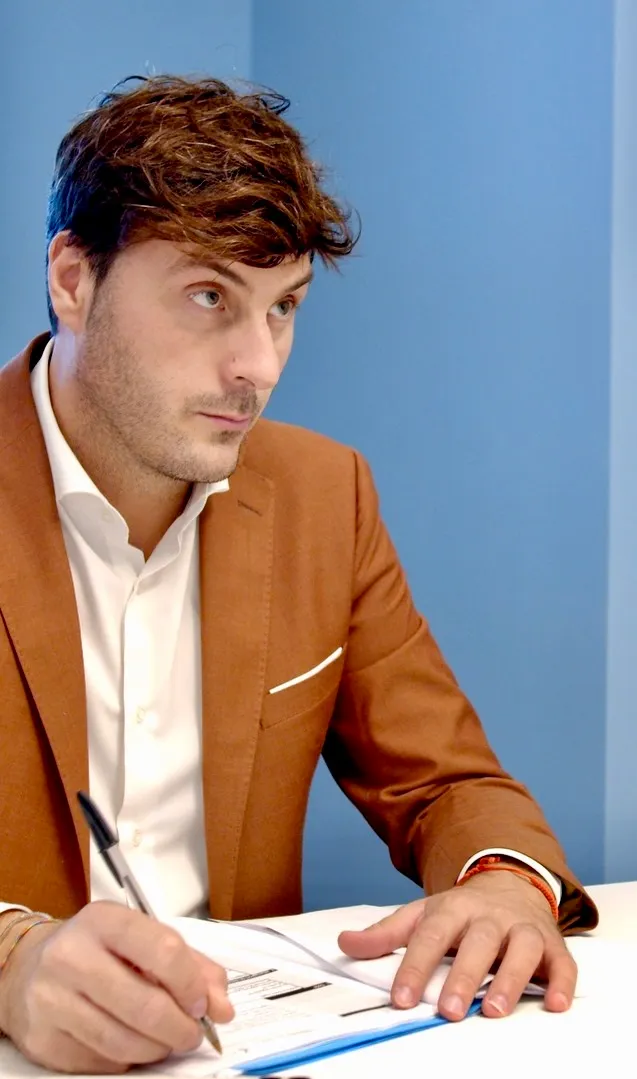 Nicola Parrinello al tavolo di lavoro, penna in mano, mentre ascolta un interlocutore